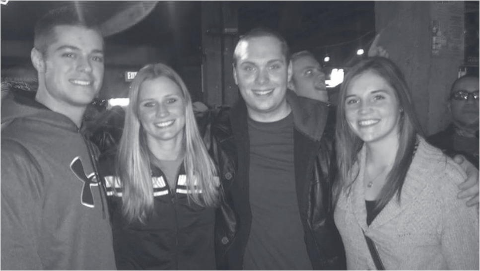 Tpr. Bava poses with three family members or friends in a dimly lit indoor setting.