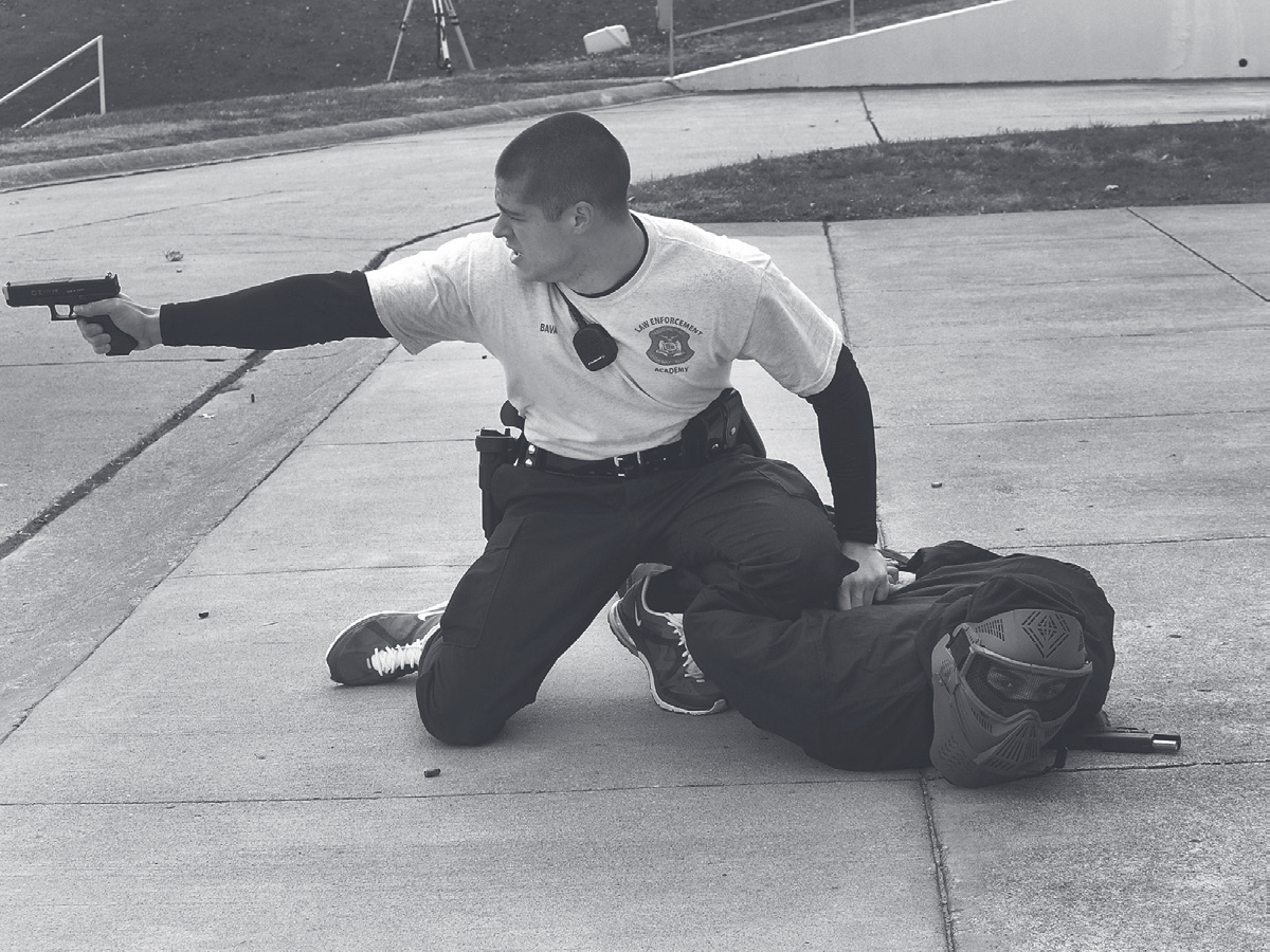 Tpr. Bava kneels in a shooting stance aiming a pistol during a firearms training exercise outdoors.