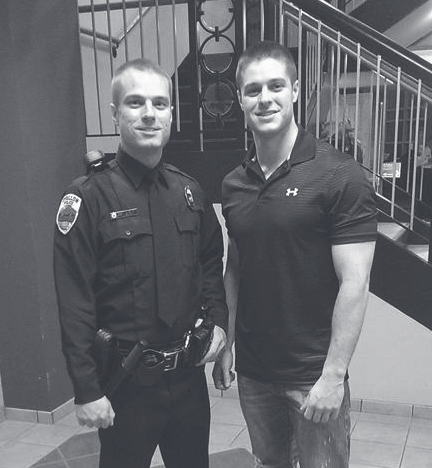 Tpr. Bava stands beside a uniformed police officer indoors near a staircase.
