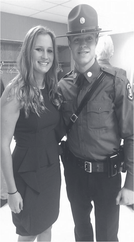 Tpr. Bava in Patrol uniform and campaign hat stands beside a woman in a dark dress indoors.