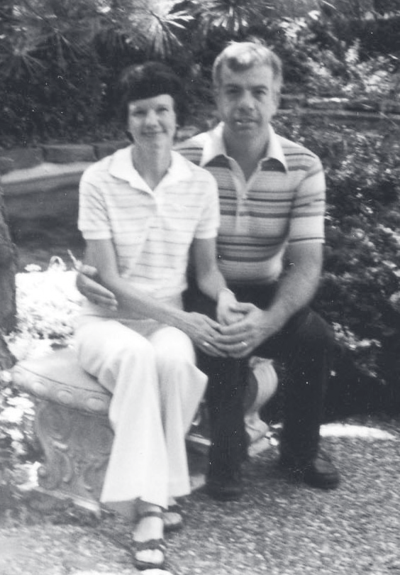 Cpl. Bruns and a woman sit together on a stone bench in a garden setting.