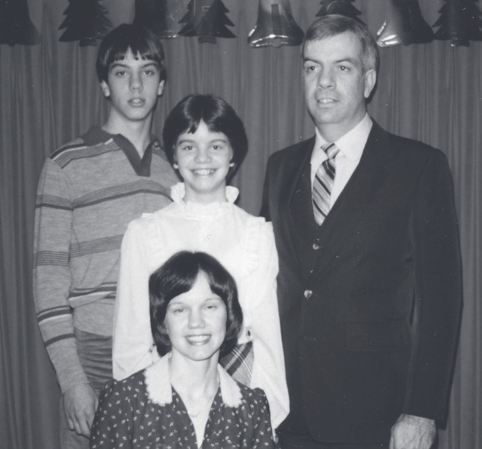Cpl. Bruns poses indoors with three family members in front of a decorated wall.