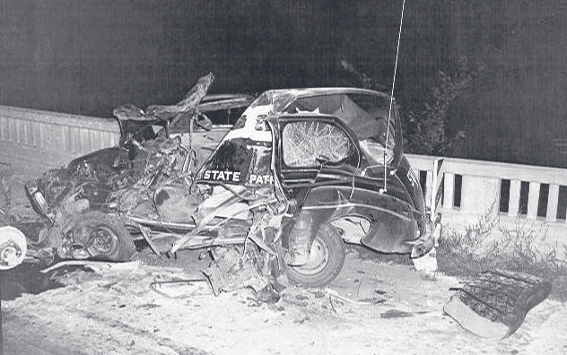 A severely wrecked and mangled automobile sits against a guardrail at night.