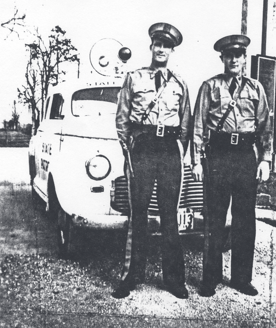 Two vintage Missouri State Highway Patrol troopers in uniform standing beside a marked State Patrol patrol car.