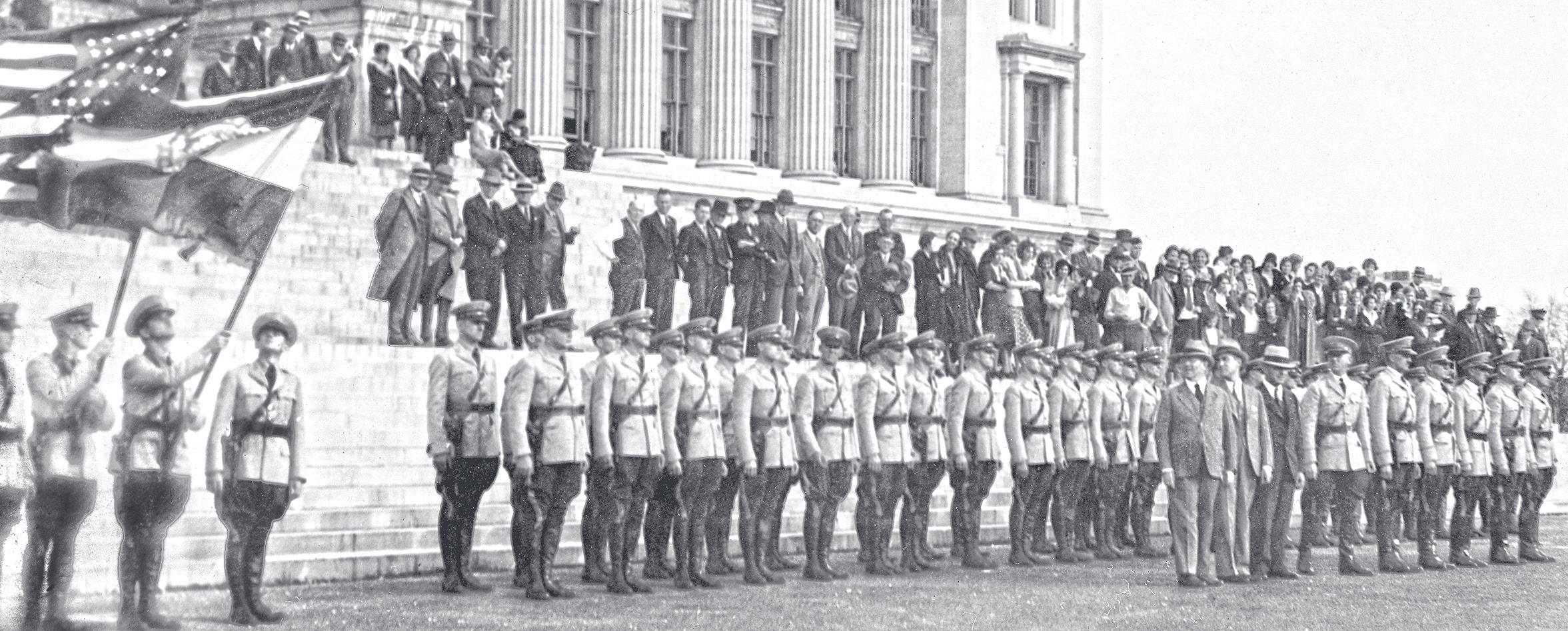 Vintage black-and-white photograph of uniformed officers standing in formation on capitol steps with flag bearers.