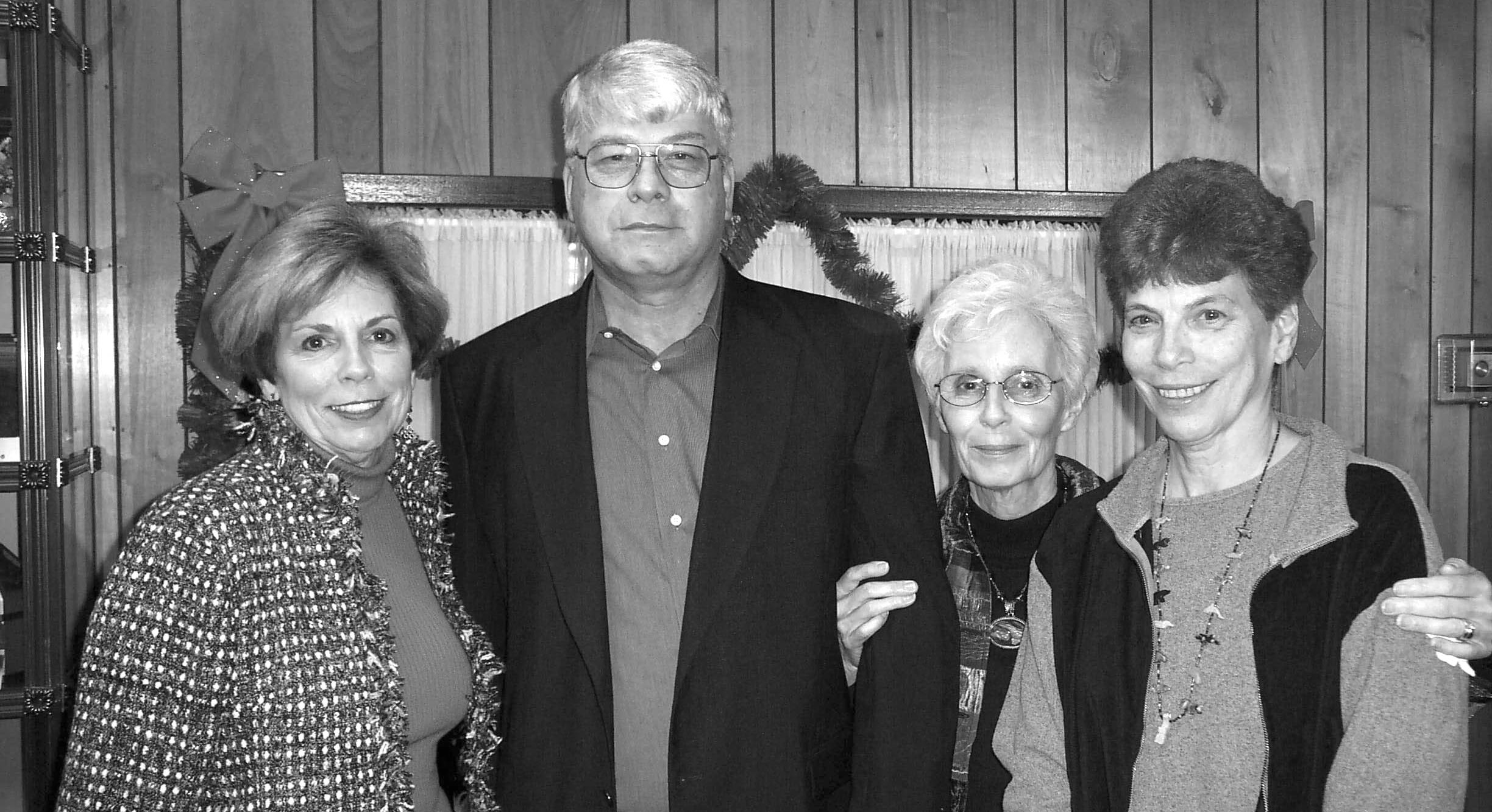 Black-and-white photograph of four family members posed together indoors in front of a wood-paneled wall.