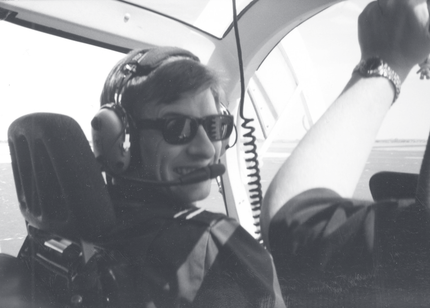 A young Cpl. Engelhard sits in an aircraft cockpit wearing sunglasses, a headset, and a shoulder harness.