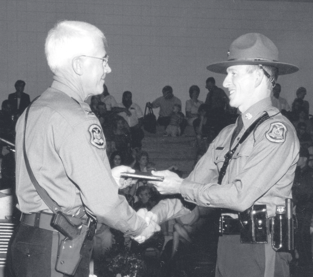 Cpl. Engelhard in uniform and campaign hat shakes hands with another officer while receiving an item at a ceremony.