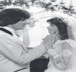 Black-and-white wedding photo showing Tpr. Floyd in a light tuxedo holding the hands of his bride wearing a lace veil and gown.