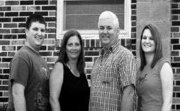 Black-and-white family portrait of Tpr. Floyd with three family members standing in front of a brick building.
