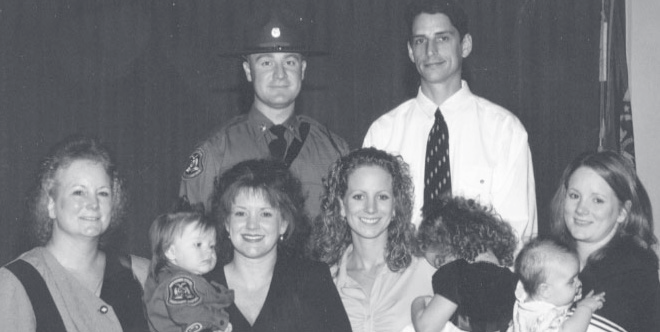 Group portrait of two uniformed officers standing behind five women and three small children posed together indoors.