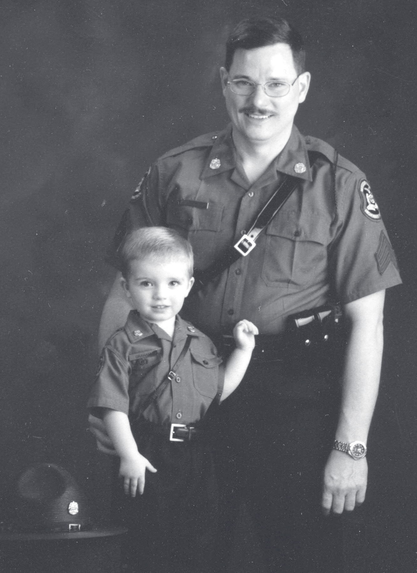 Sgt. Graham in uniform poses with a young child wearing a matching uniform, campaign hat resting beside them.