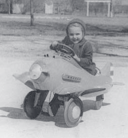 Vintage black-and-white photo of a smiling young child in a toy airplane.