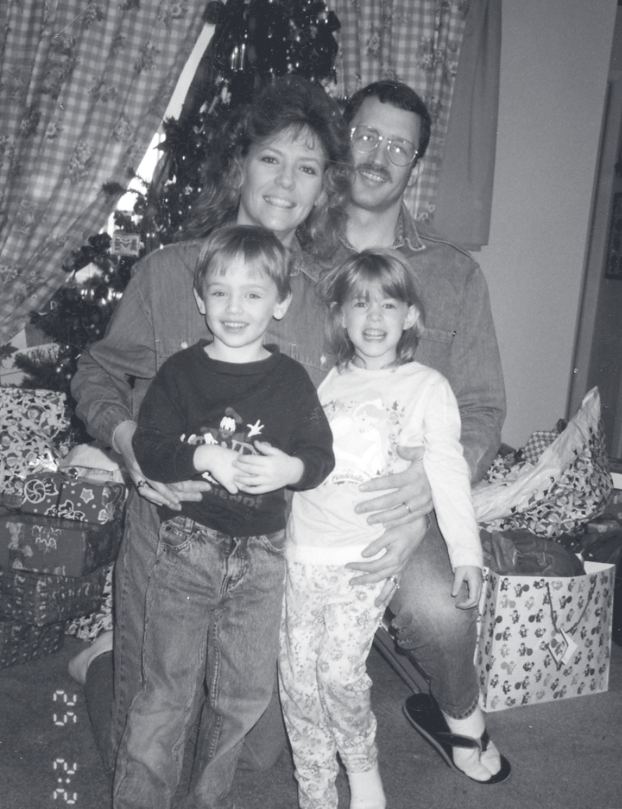 Sgt. Guilliams, a woman, and two young children pose in front of a Christmas tree with presents.