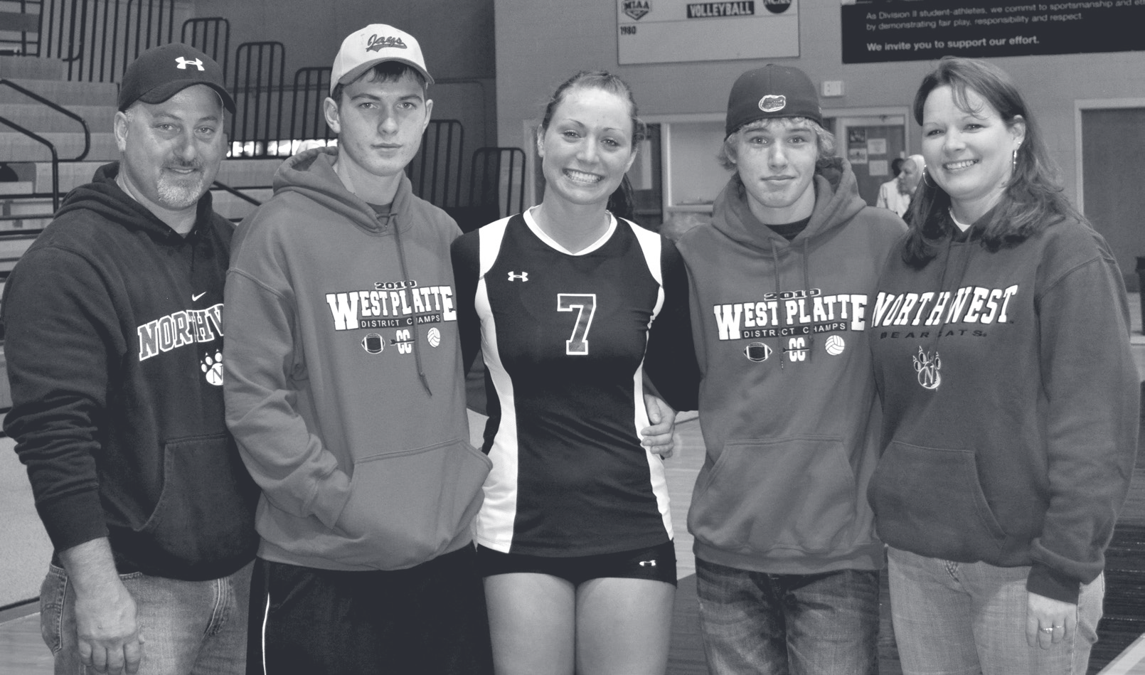 Tpr. Guthrie stands with four family members at a school gymnasium wearing sweatshirts and volleyball attire.