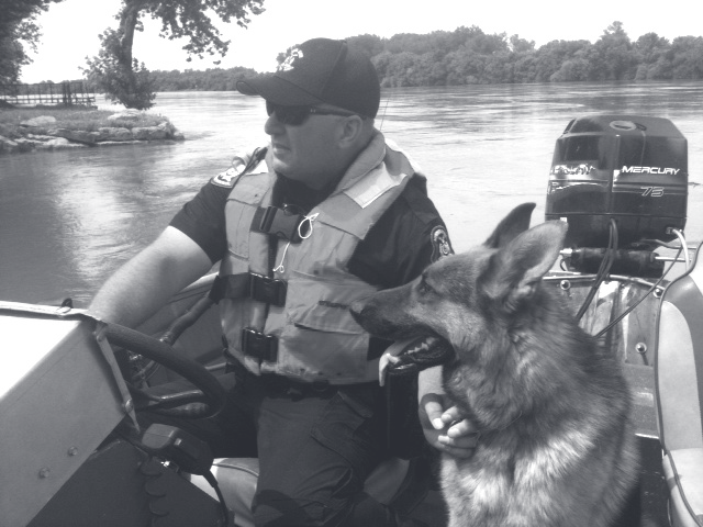 Tpr. Guthrie sits in a boat on a river wearing a life vest alongside his German Shepherd K-9 partner.