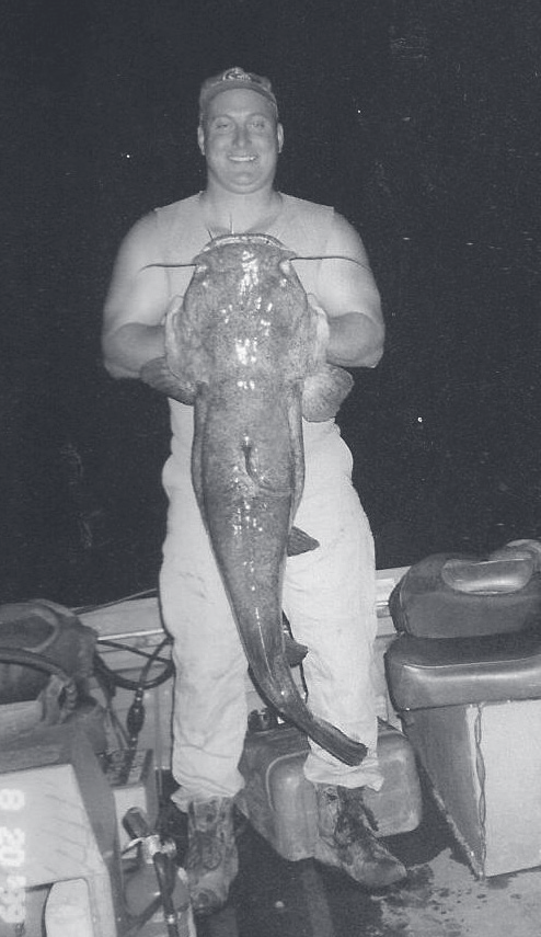 Tpr. Guthrie holds up a large fish while standing on a boat at night.