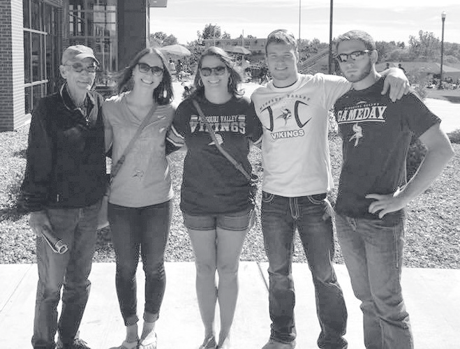 Five family members stand together outdoors wearing casual sweatshirts and sunglasses.