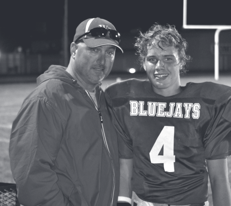 Tpr. Guthrie poses on a football field at night with a young player wearing a Bluejays number 4 jersey.