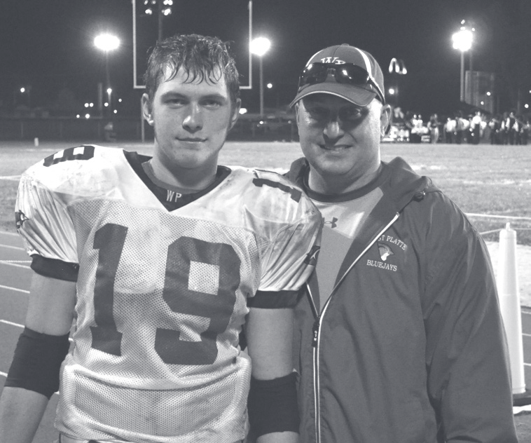Tpr. Guthrie poses on a football field at night with a young player wearing a number 19 jersey.