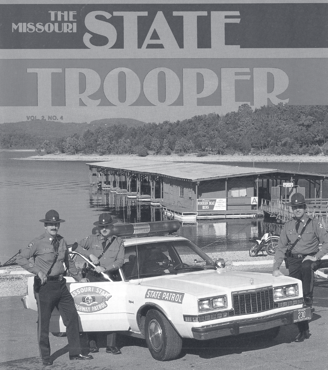 Three troopers in campaign hats pose with a marked patrol car on a lakeshore, boat dock behind them, on a Missouri State Trooper magazine cover.