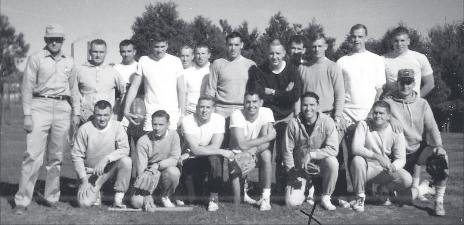 Large group of young men in athletic clothing posed together outdoors on a grassy field.