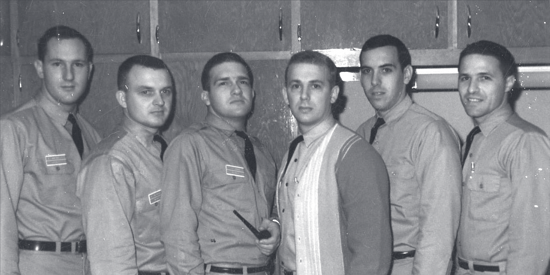 Tpr. Jenkins stands in a group of six men, five in uniform, inside a locker room.