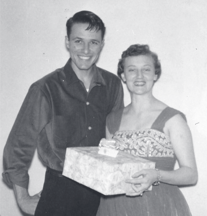 Tpr. Jenkins and a woman stand together indoors holding a wrapped gift box.