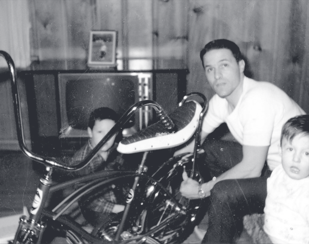 Tpr. Jenkins sits on the floor beside a motorcycle with two young children in a living room.