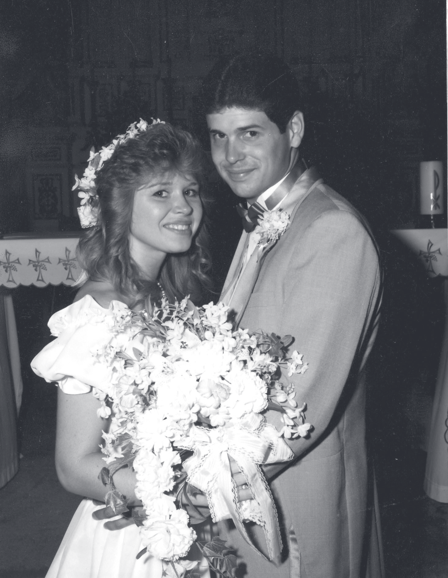 Tpr. Kolilis in a light suit poses with a bride holding a large floral bouquet at a wedding.
