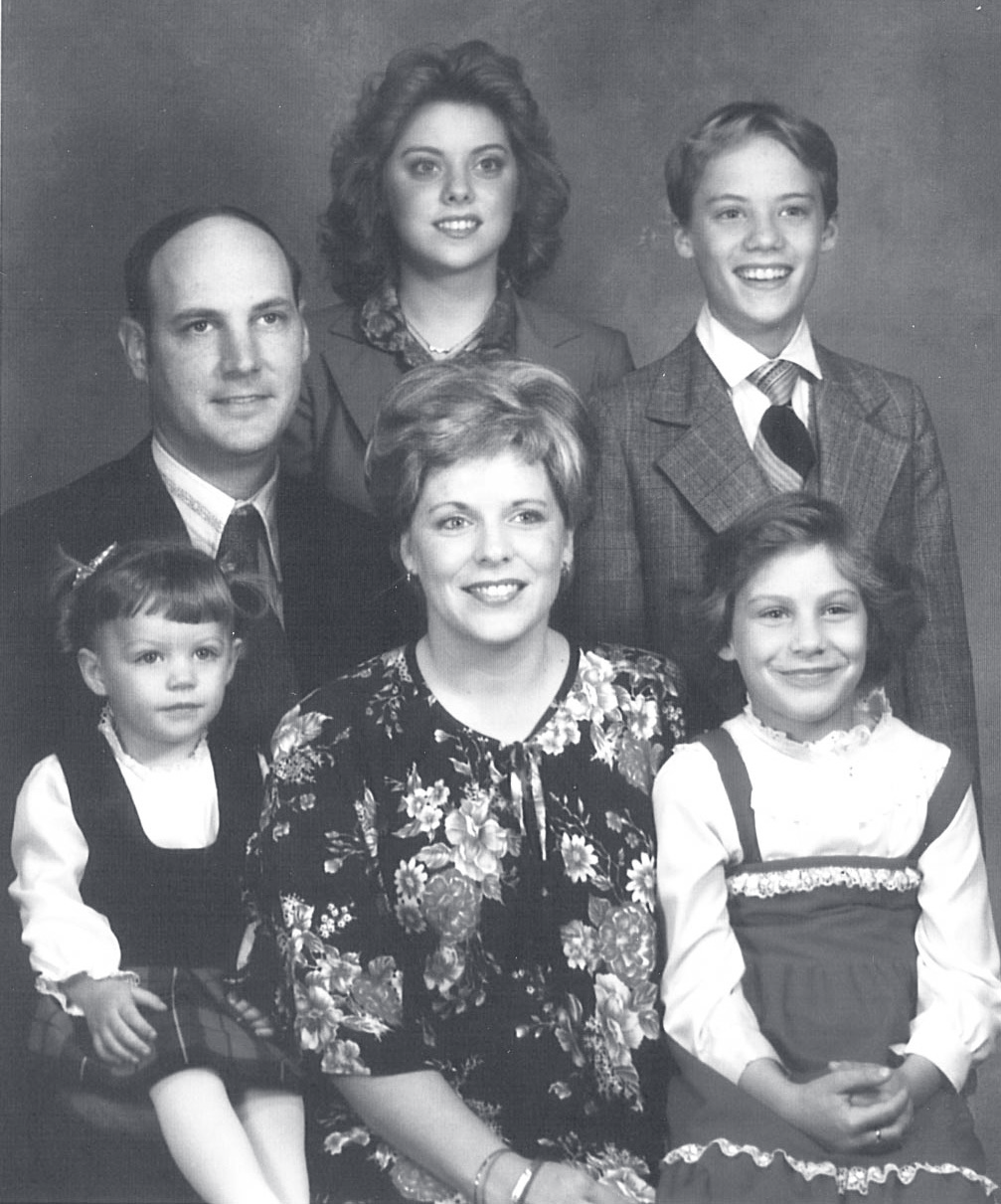 Black-and-white family portrait of a man, woman, and four children posed together in studio attire.