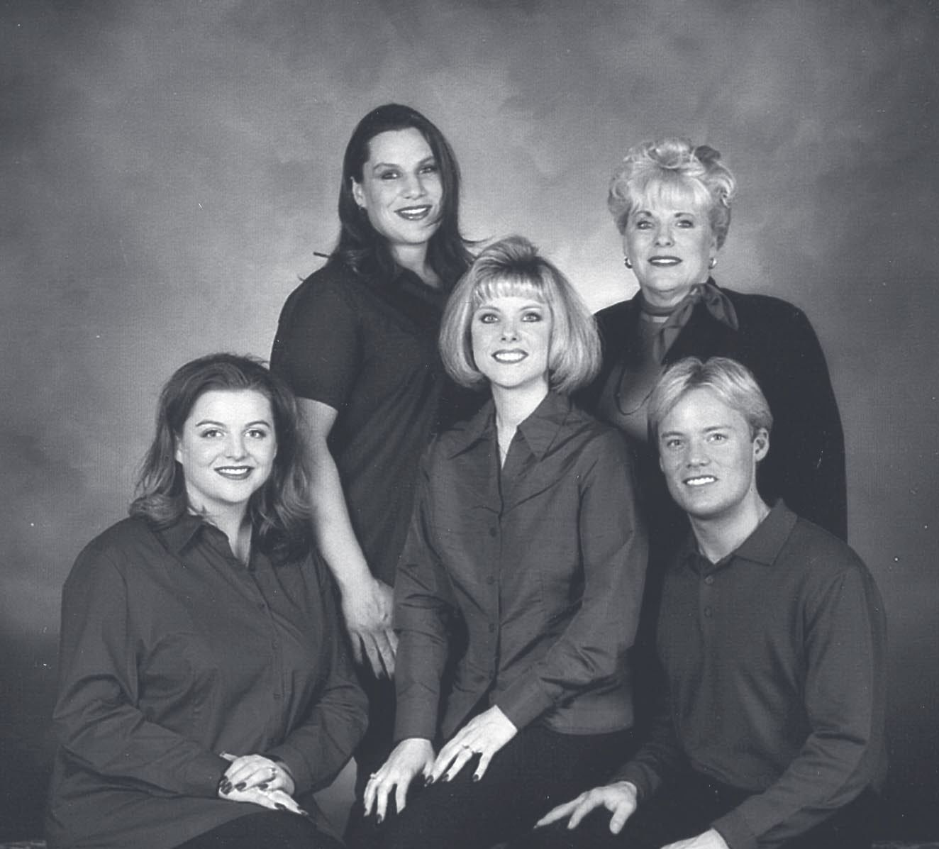 Black-and-white studio portrait of five adults wearing dark shirts, posed together against a neutral backdrop.