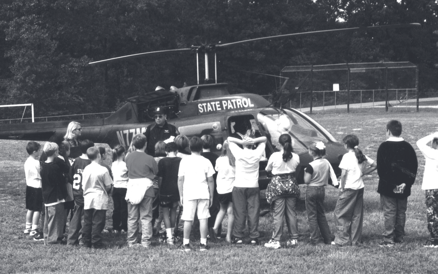 A uniformed trooper stands beside a State Patrol helicopter while a group of children gather around to view it.