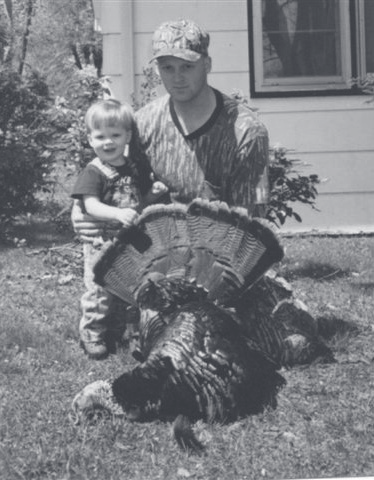 Tpr. Poynter kneels in a yard wearing camouflage alongside a young child and a harvested wild turkey.