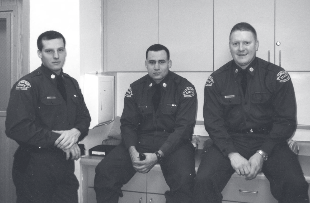 Three uniformed officers sit together on a counter in an indoor room, posing for a group photo.