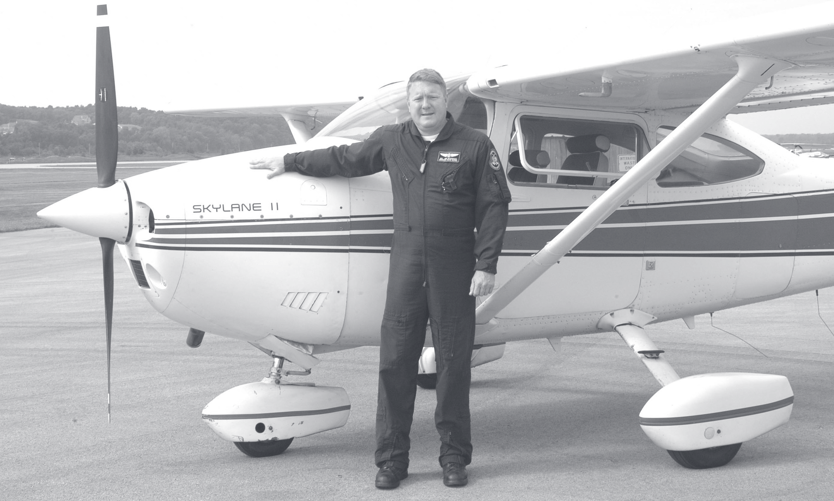 Sgt. Schuengel in a flight suit leans against a Skylane II single-engine airplane parked on a tarmac.