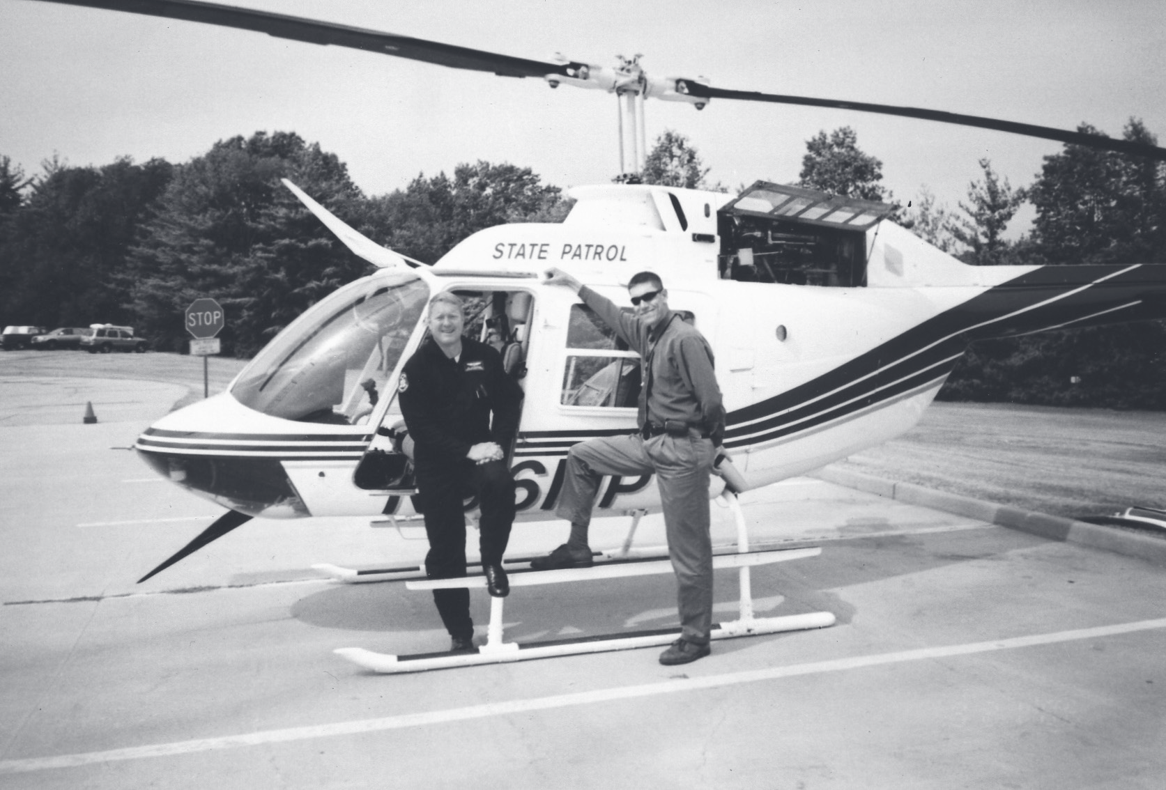 Sgt. Schuengel and another officer pose on the skids of a State Patrol helicopter parked in a lot.