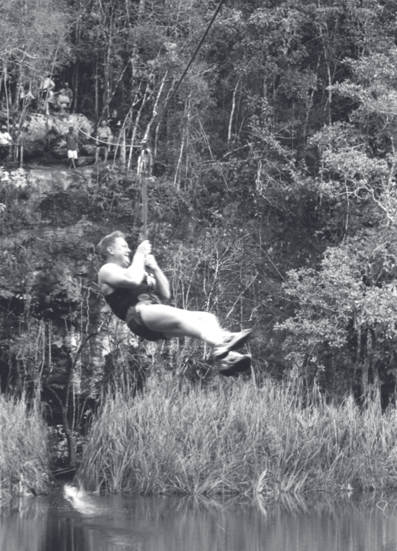 Sgt. Schuengel swings on a rope swing over a pond surrounded by trees and tall grass.