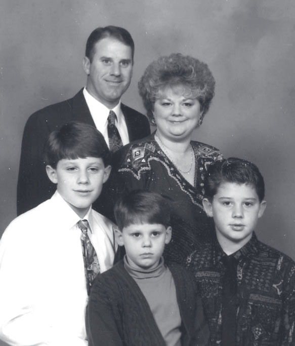 A studio family portrait of a man, woman, and three children posed together against a dark backdrop.