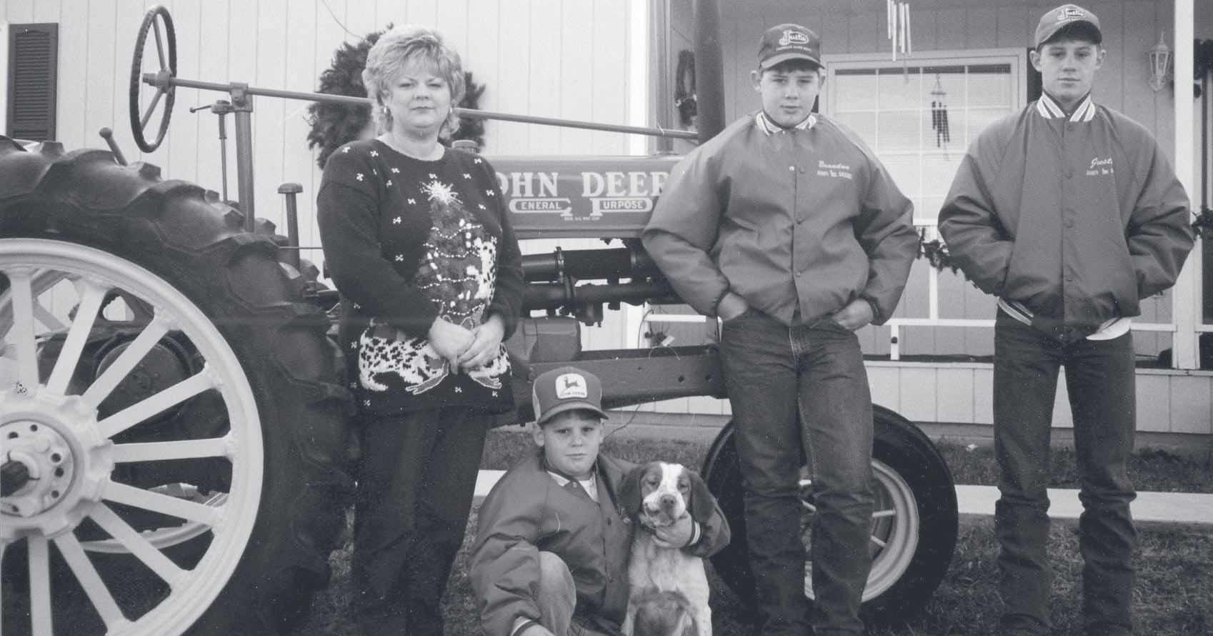 A woman, two young men in matching jackets, and a boy with a dog pose beside a John Deere tractor.