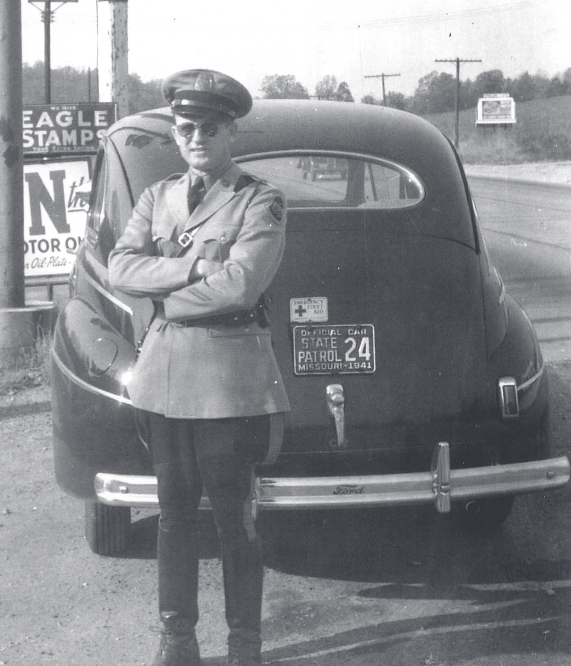 Tpr. Walker in uniform and cap stands with arms crossed beside a 1941 Missouri State Patrol vehicle.