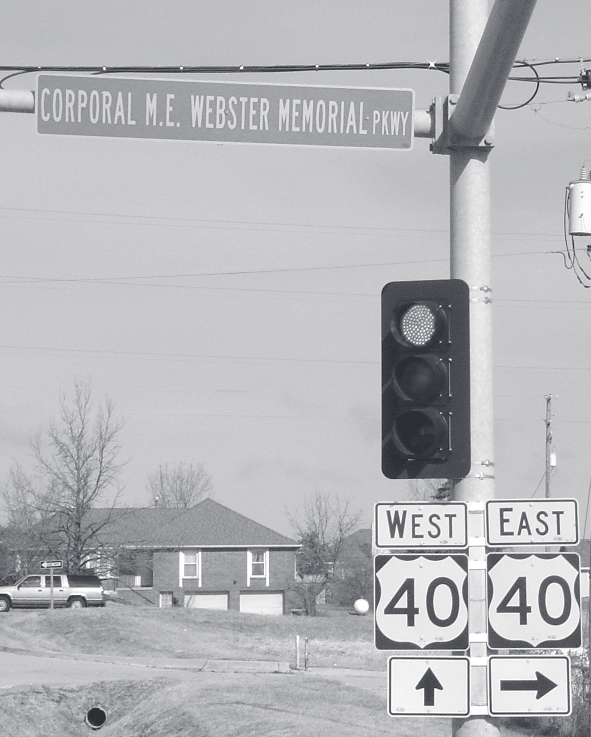 Street sign reading 'Corporal M.E. Webster Memorial Pkwy' mounted above a traffic signal at the intersection of West and East U.S. Route 40.